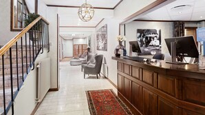A hotel lobby with a reception desk, seating area, and a staircase.