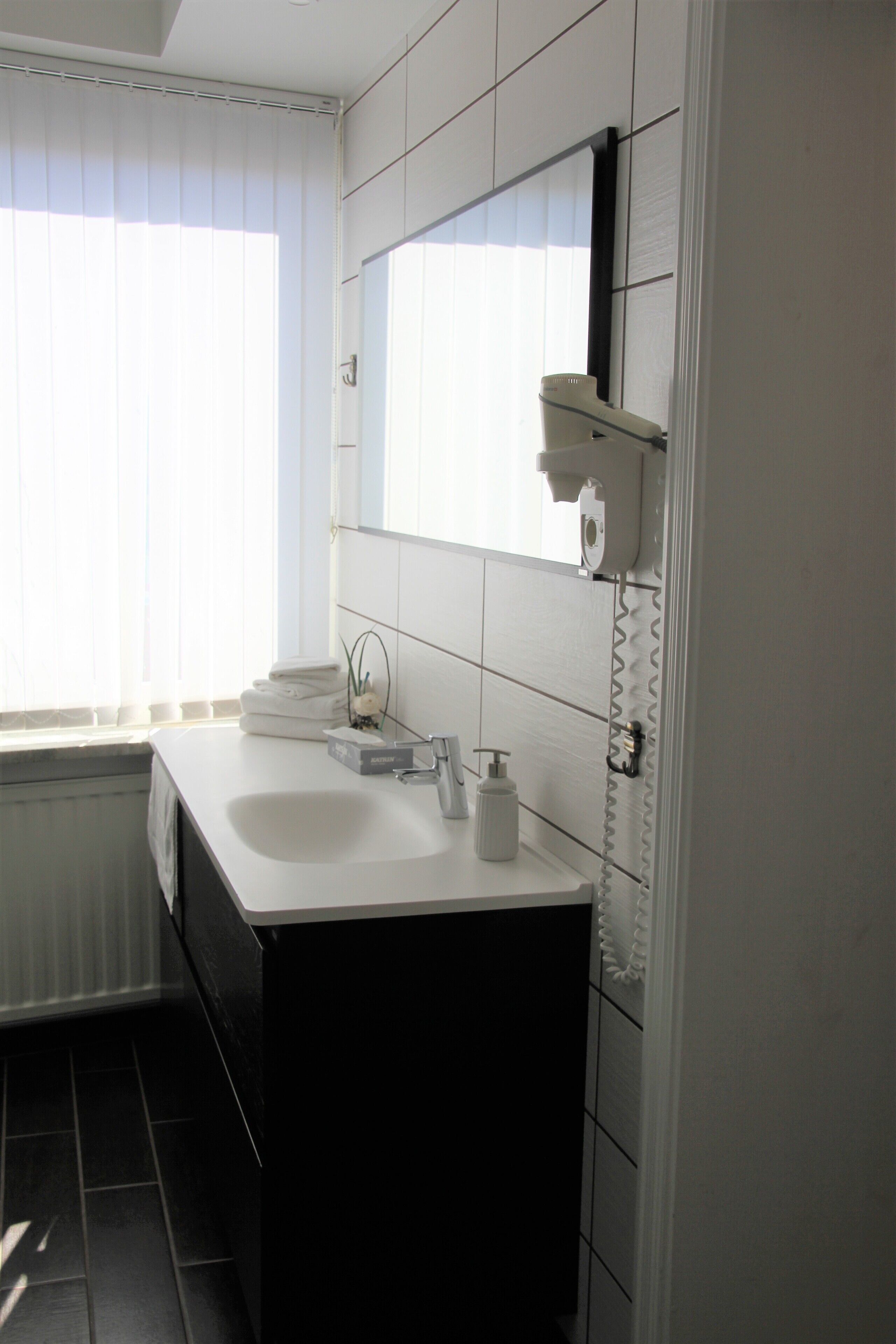 Ein modernes Badezimmer mit einem weißen Waschbecken, einem Spiegel und einem Fenster mit Jalousien.