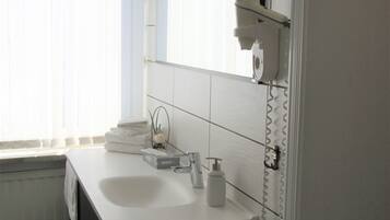 Ein modernes Badezimmer mit einem weißen Waschbecken, einem Spiegel und einem Fenster mit Jalousien.