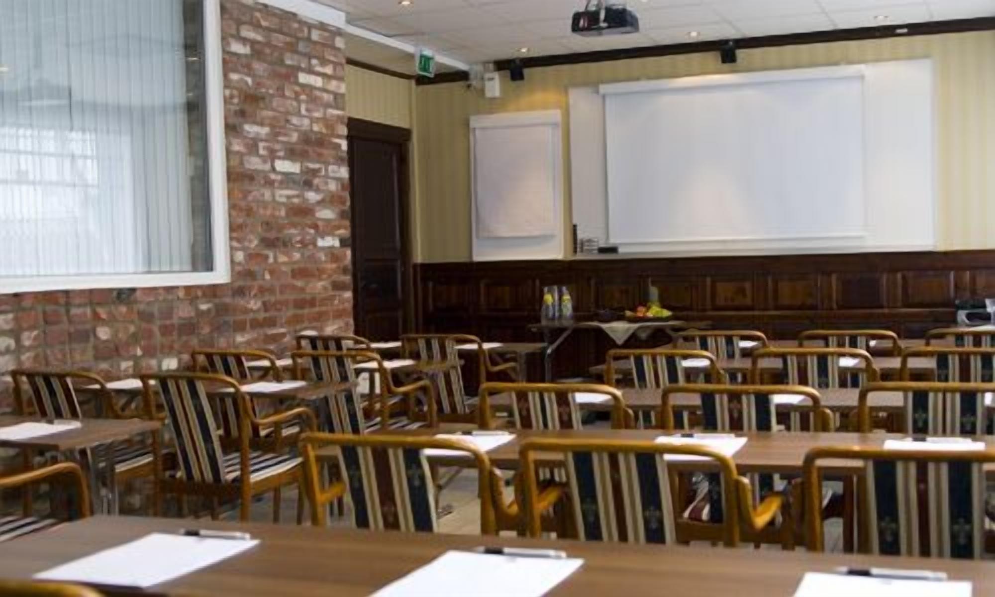 A conference room with wooden tables and chairs, a brick wall, and a whiteboard.