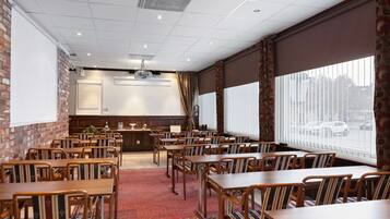 A conference room with multiple tables and chairs, a projector, and a large window with blinds.