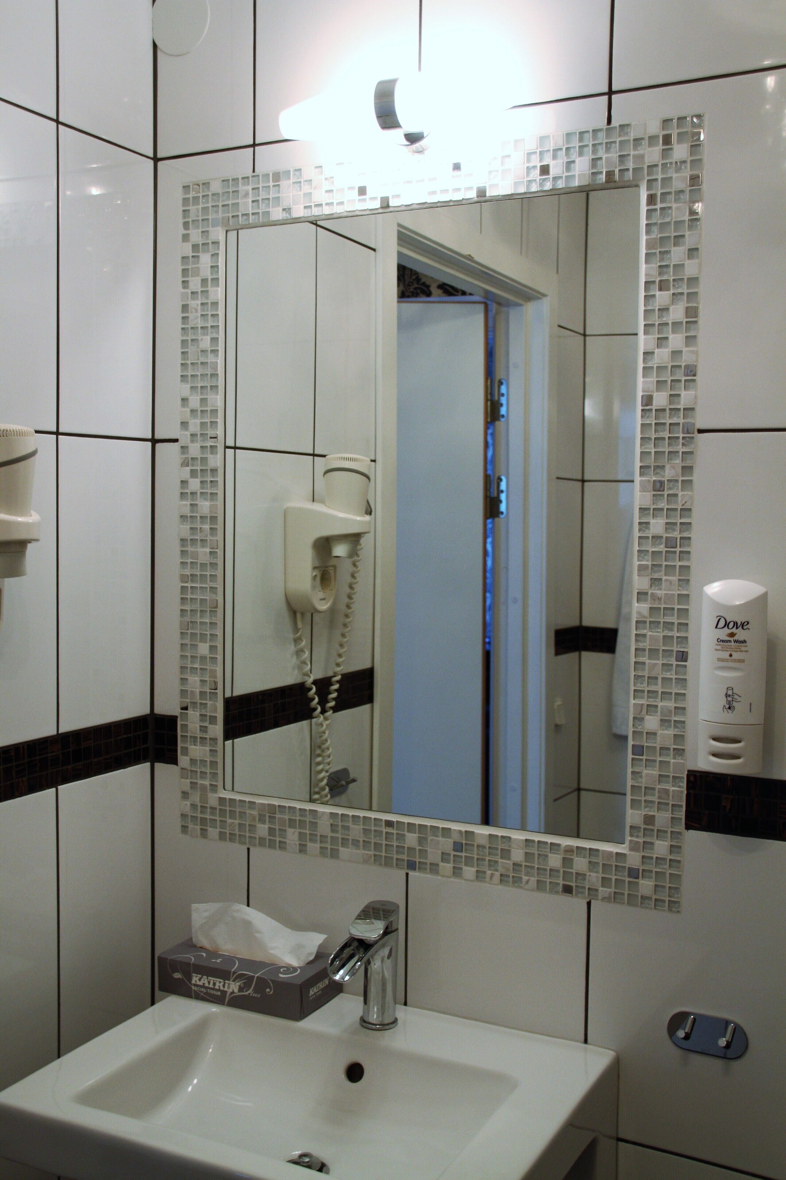 A bathroom with a white sink, a mirror with mosaic tiles, a hairdryer, and a Dove lotion dispenser.