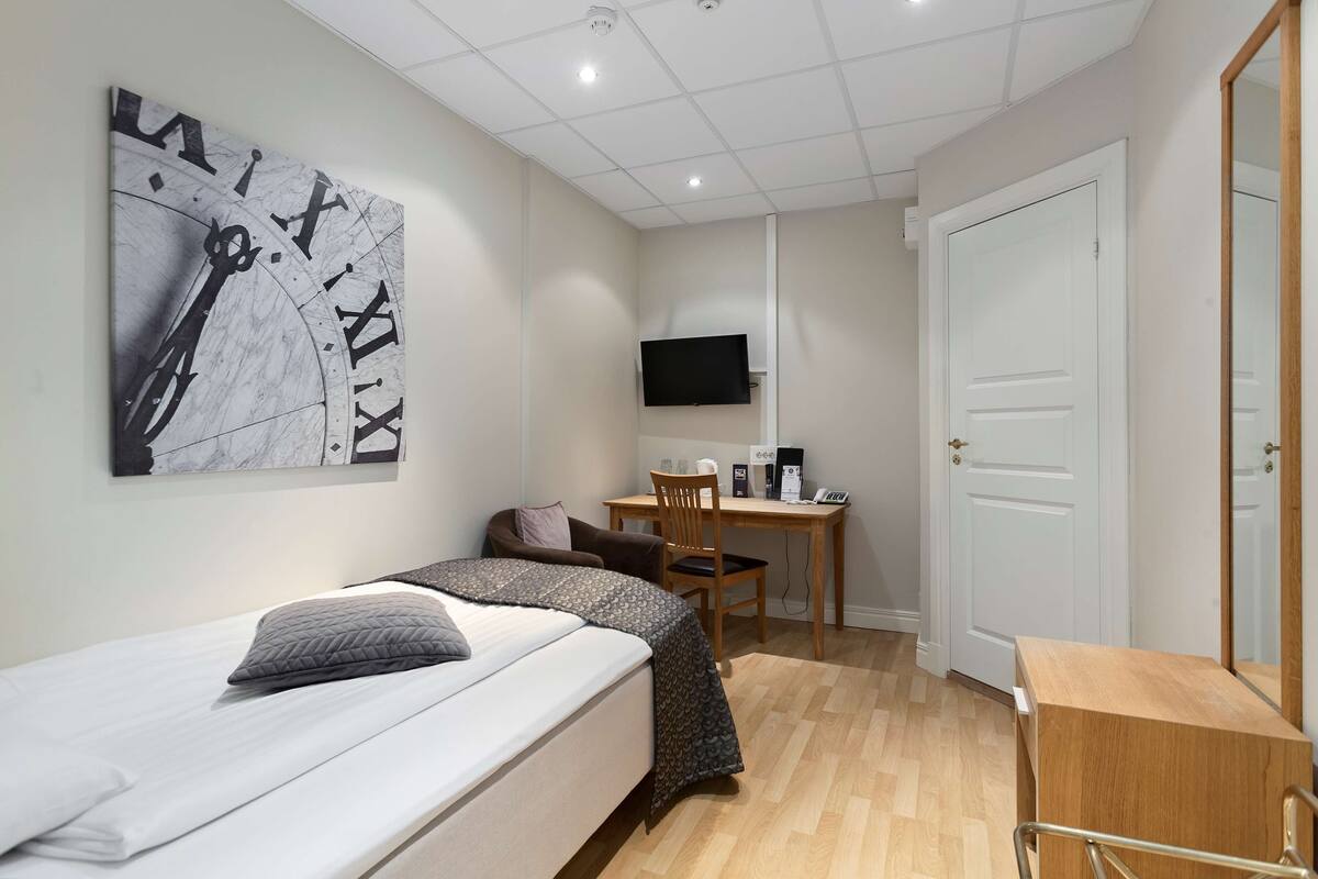 A bedroom with a bed, a desk, a chair, a TV, and a door.