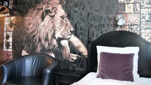 A bedroom with a large lion mural on the wall, a black leather chair, a bed with white and purple pillows, and a patterned wall.