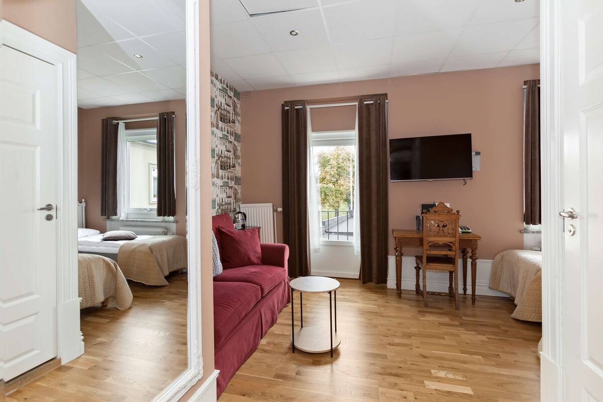 A room with a red sofa, a round table, a TV, and a bed with a window view.