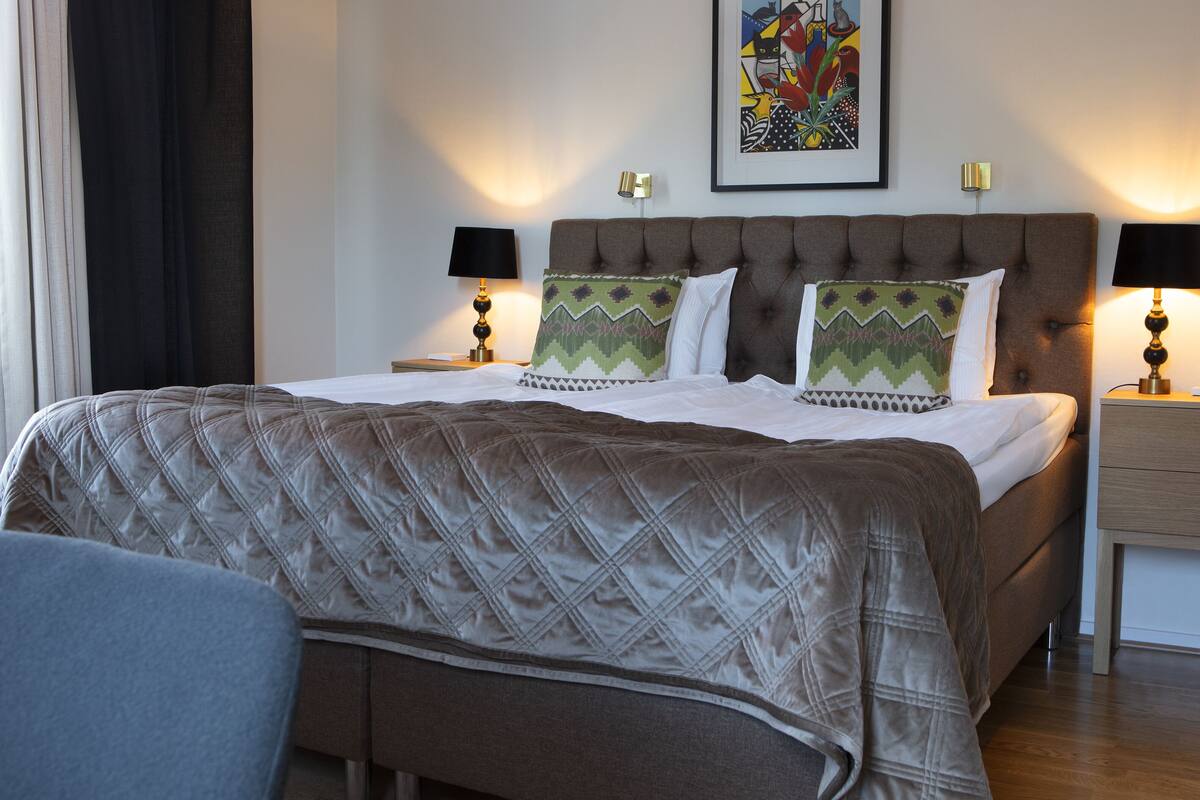 A neatly made bed with a quilted headboard, two bedside lamps, and a framed artwork on the wall.