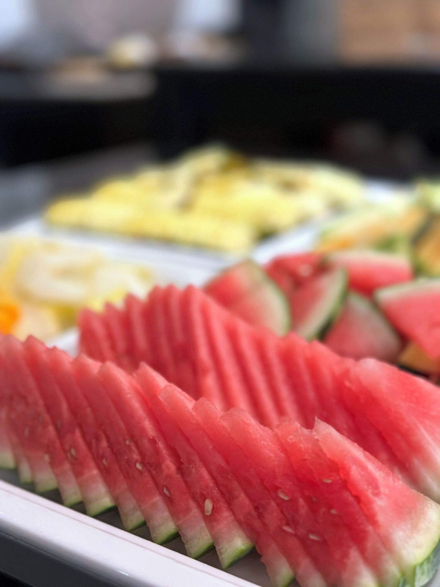A close-up of a watermelon slice with a serrated edge, placed on a white plate.