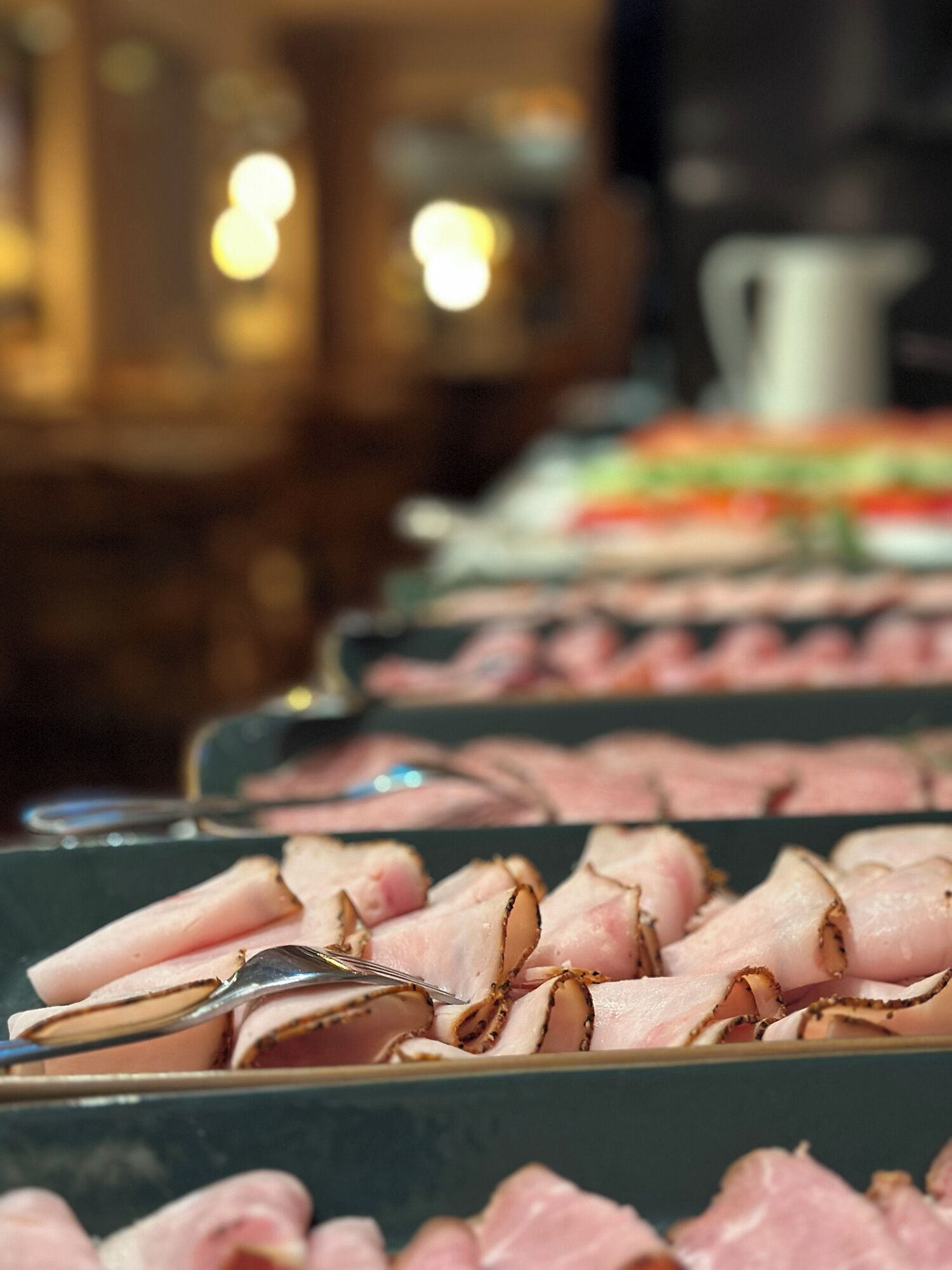 A buffet with sliced meats and a pitcher in the background.