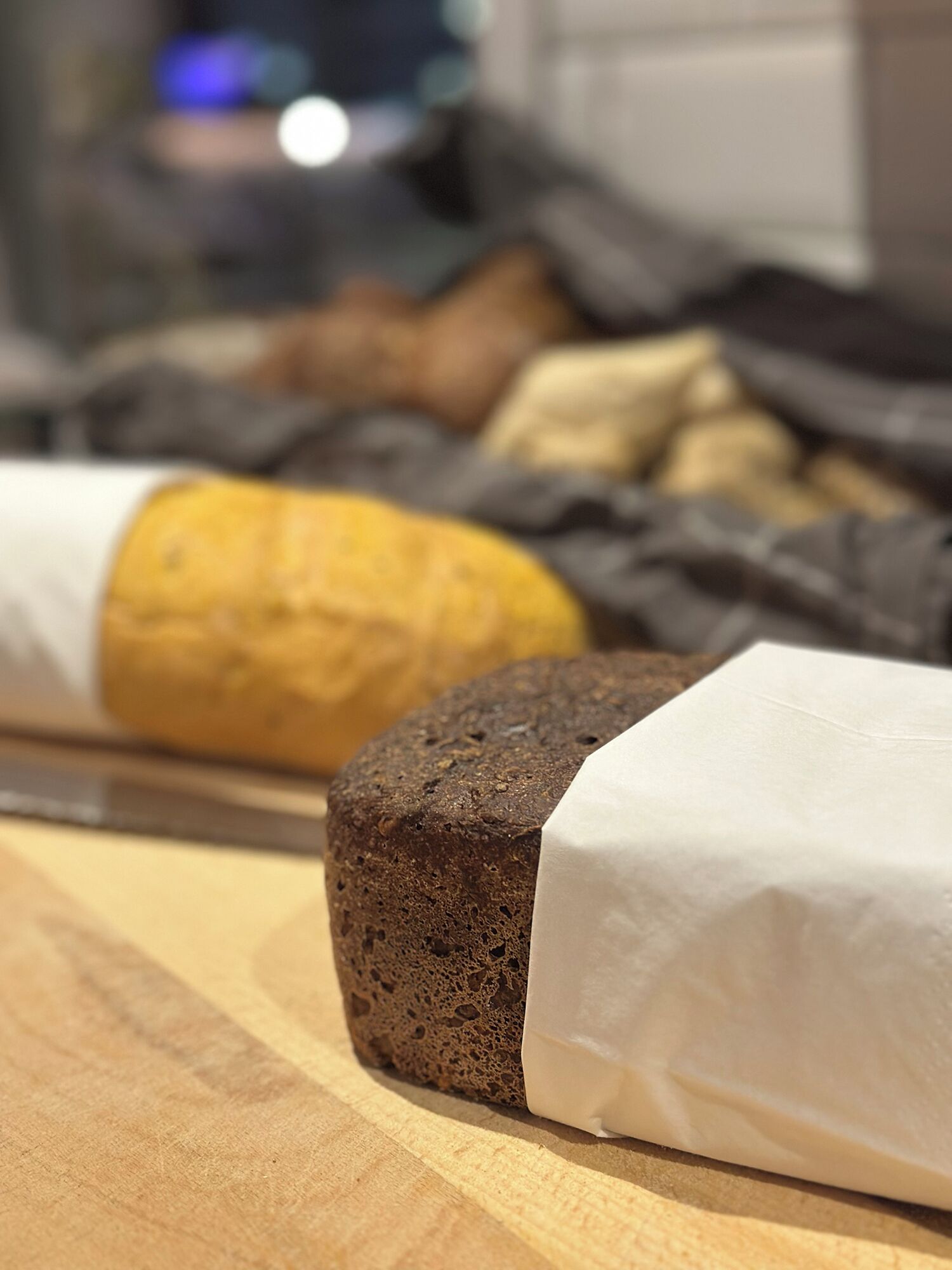 A loaf of bread wrapped in white paper on a wooden surface.