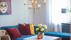 Una sala de estar con un sofá azul, un sillón color beige, una mesa de centro y un tapete colorido.
