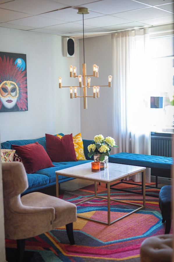 A living room with a blue sofa, a beige armchair, a coffee table, and a colorful rug. - Mjolby Stadshotell (Mjolby)