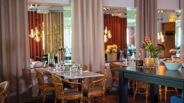 Un restaurante con sillas y mesas de madera, velas y flores sobre las mesas.
