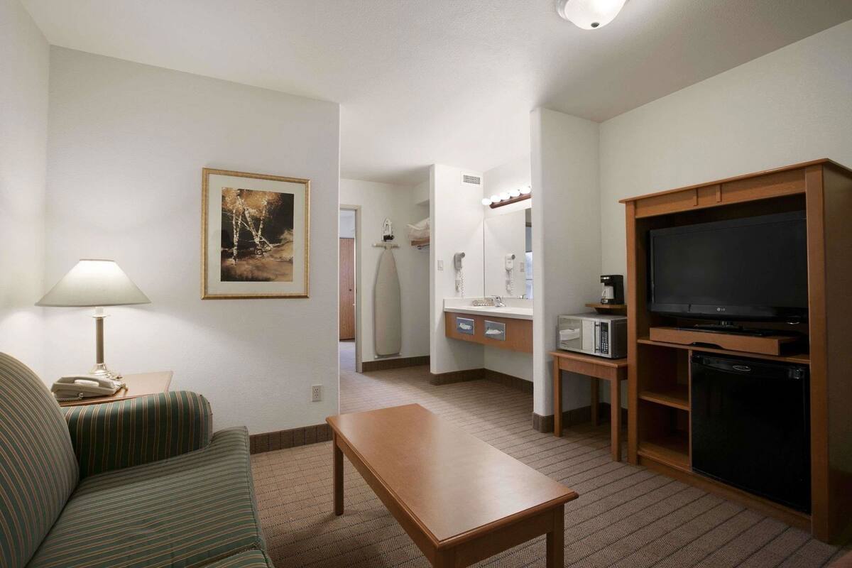 Habitació d'hotel amb un llit, televisió, microones, cafetera, làmpada, un quadre amb marc i un bany amb rentapla i mirall.