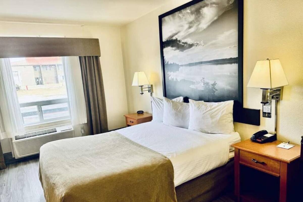 Habitació d'hotel amb un llit gran, dues làmpades laterals, una tauleta de nit i una finestra amb cortines.