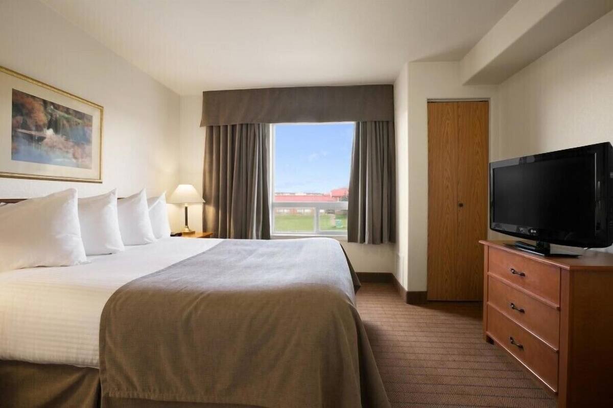 Habitació d'hotel amb un llit, una televisió sobre una petita taula de nit de fusta, una finestra amb cortines i un quadre penjat a la paret.