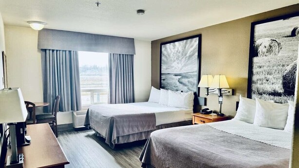 Habitación de hotel con dos camas, un escritorio, una silla, una lámpara y un amplio ventanal con cortinas.
