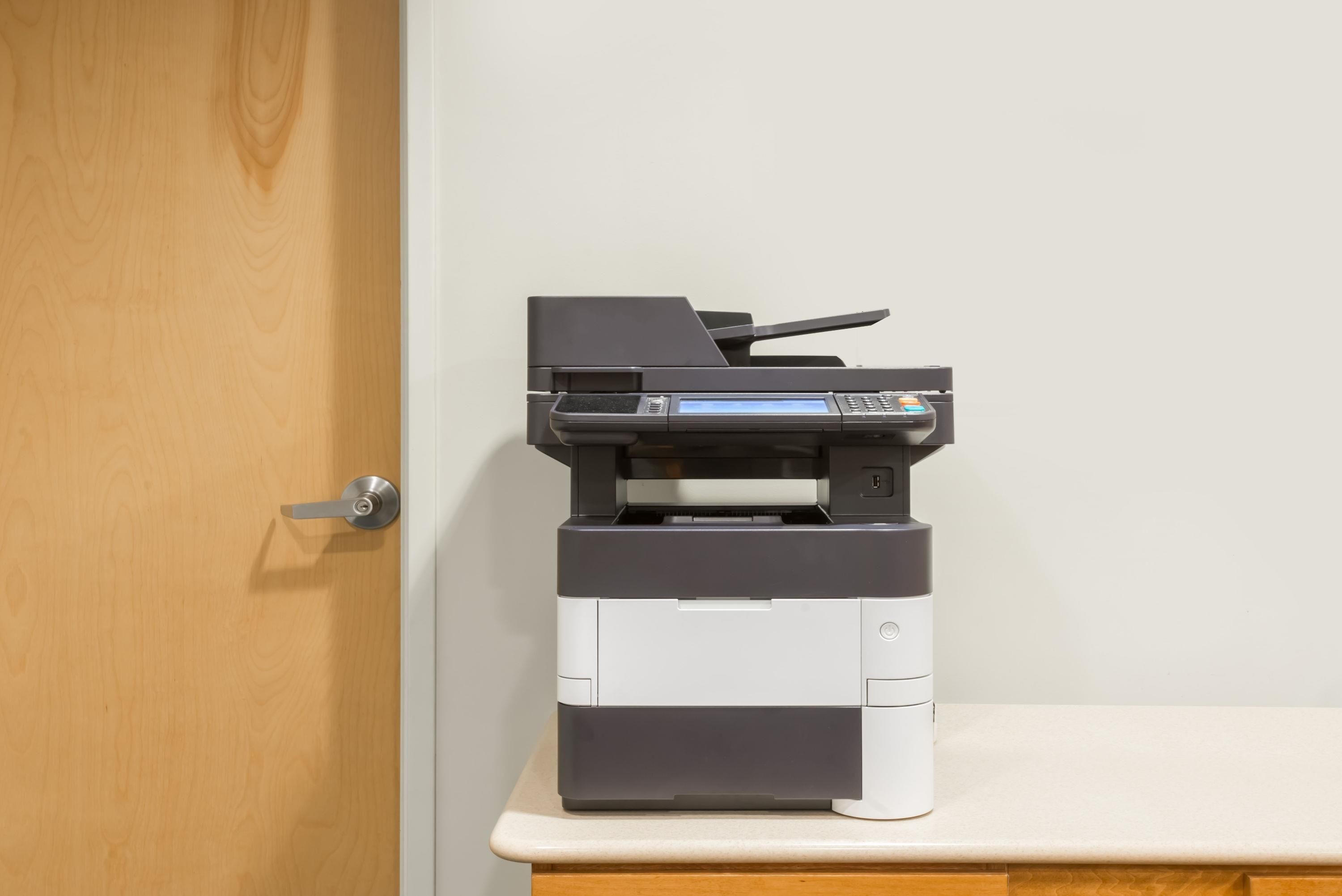 A printer on a desk next to a wooden door.