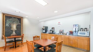 A dining area with a wooden table and chairs, a painting on the wall, and a kitchenette with a coffee machine and microwave. - Super 8 by Wyndham Hagerstown/Halfway Area (Hagerstown)