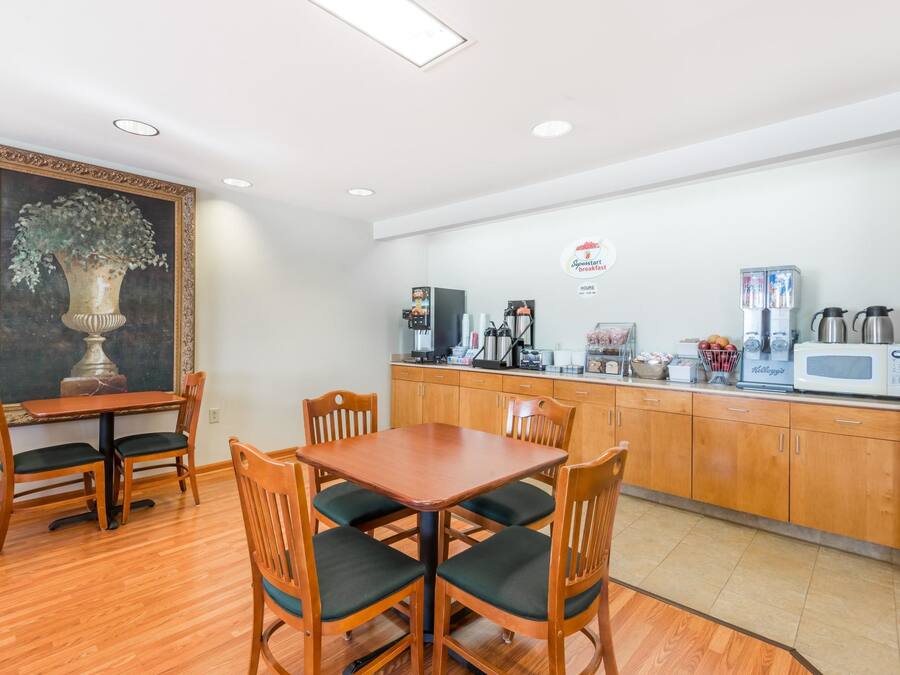 A dining area with a wooden table and chairs, a painting on the wall, and a kitchenette with a coffee machine and microwave.