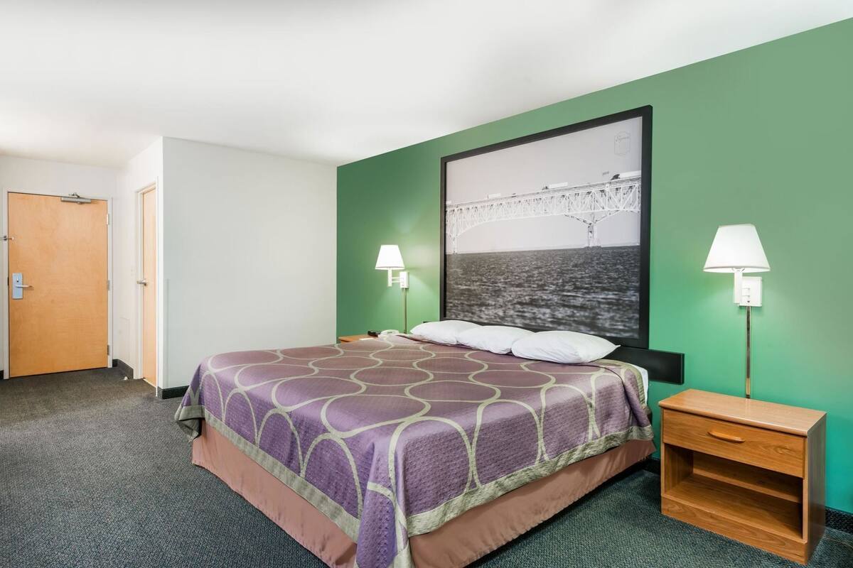 A hotel room with a bed, two bedside tables, a nightstand, a green wall, and a framed picture above the bed.