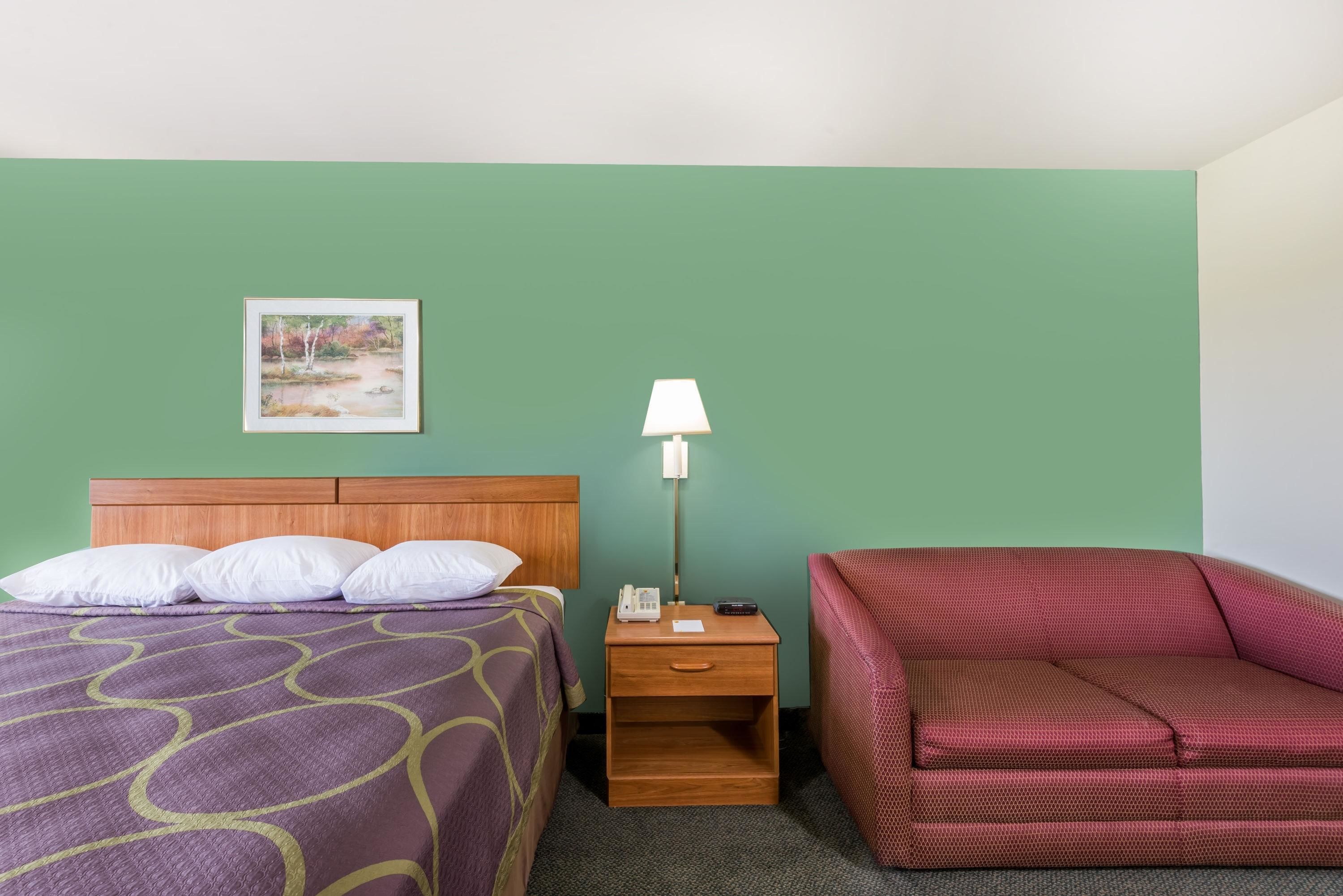 Een hotelkamer met een bed, een nachtkastje met een lamp en een rode bank.