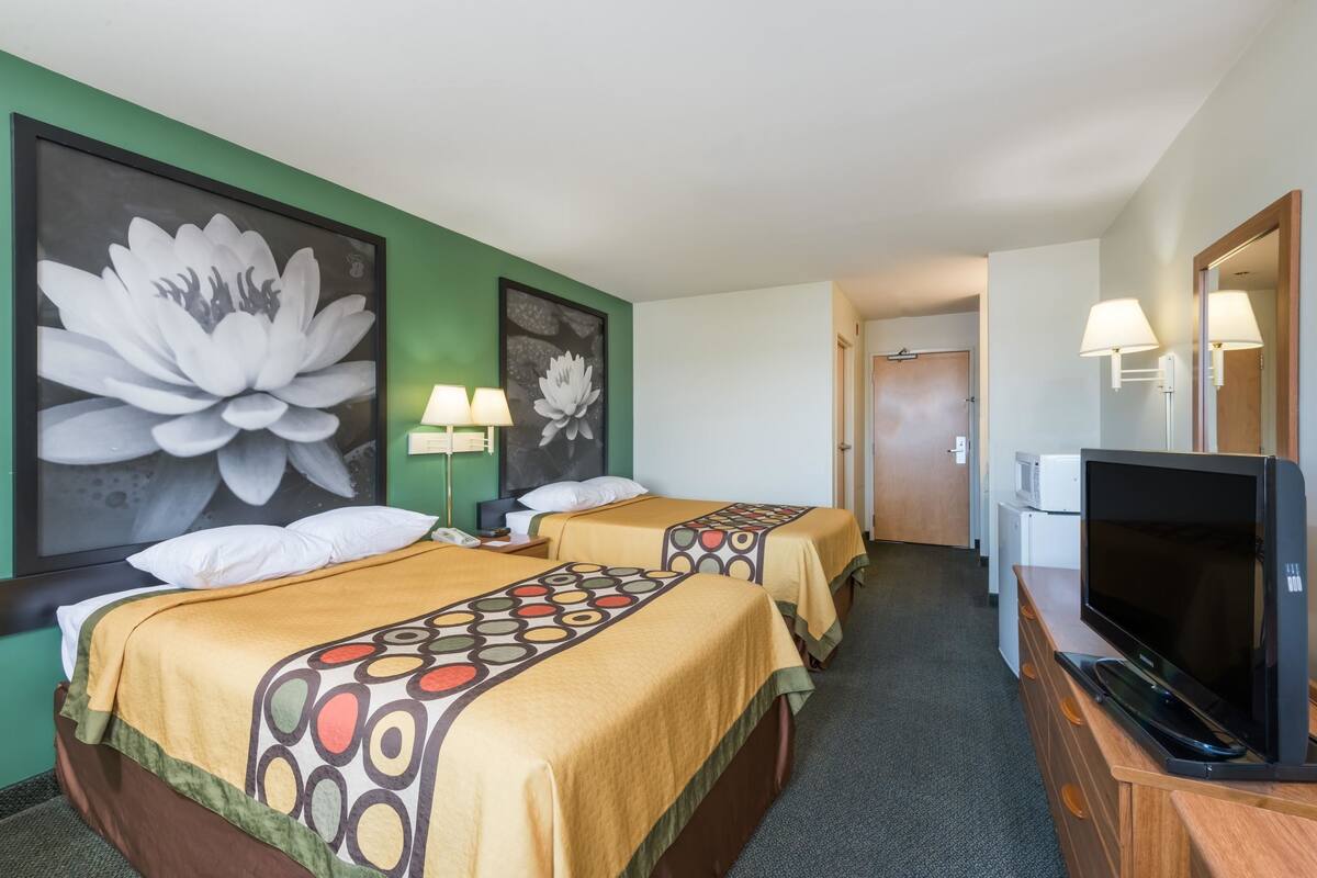 A hotel room with two beds, a TV, a desk, and a microwave.