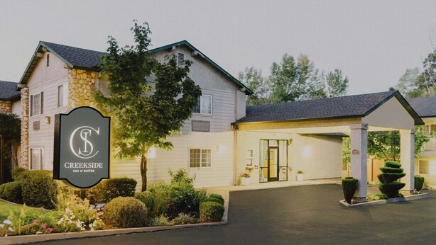 A Creekside Inn & Suites with a stone facade, a covered entrance, and well-maintained landscaping. - Creekside Inn & Suites (Willits)