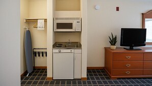A compact kitchenette with a microwave, stove, and dishwasher, a small ironing board, and a television on a wooden dresser. - Creekside Inn & Suites (Willits)