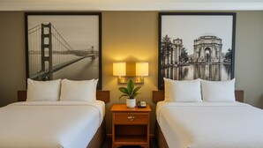A hotel room with two beds, a nightstand with a lamp and a plant, and two framed pictures on the wall. - Creekside Inn & Suites (Willits)