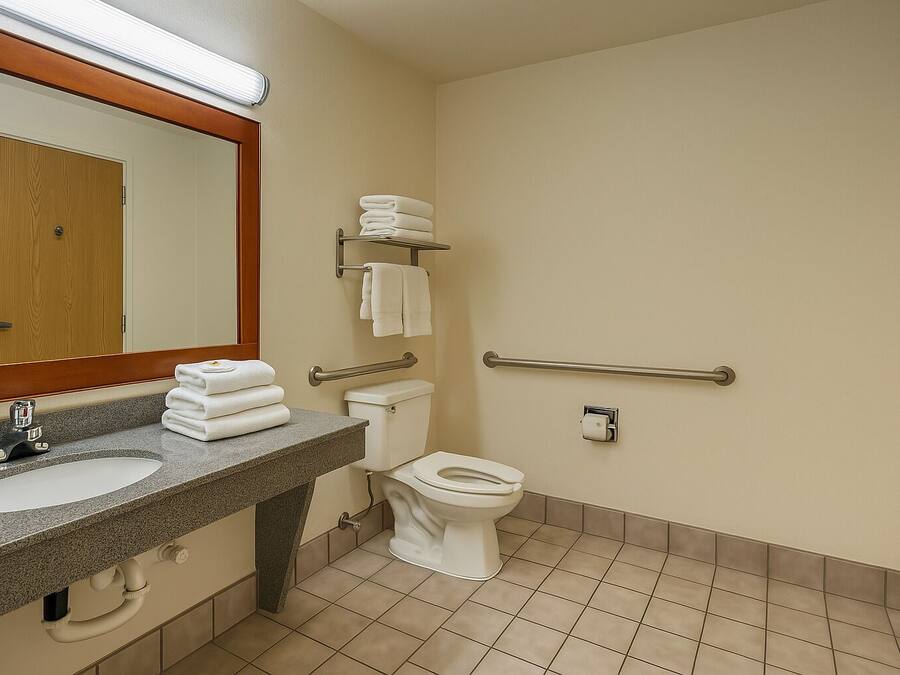 Un baño con lavamanos, espejo, inodoro y barras de apoyo.