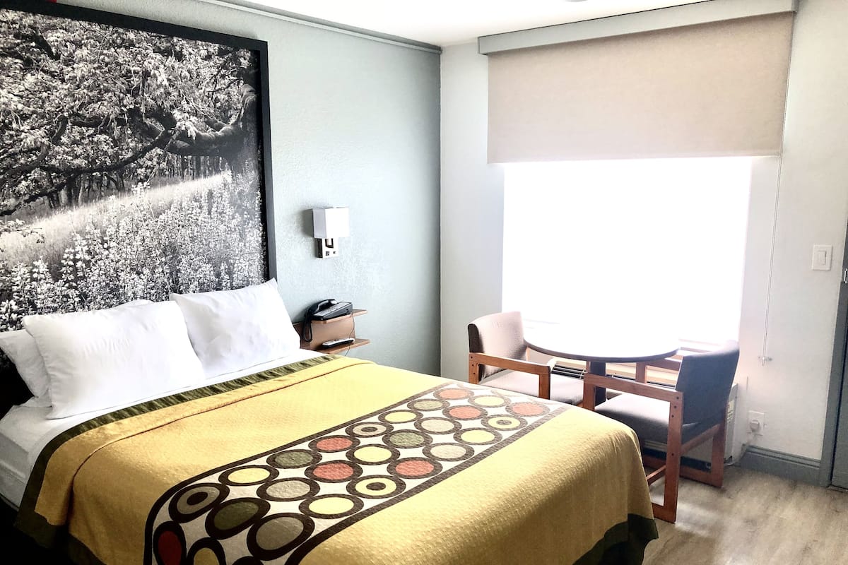 Ein Hotelzimmer mit Bett, Schreibtisch mit Stuhl, Fenster mit Aussicht und einem an der Wand befestigten Telefon.