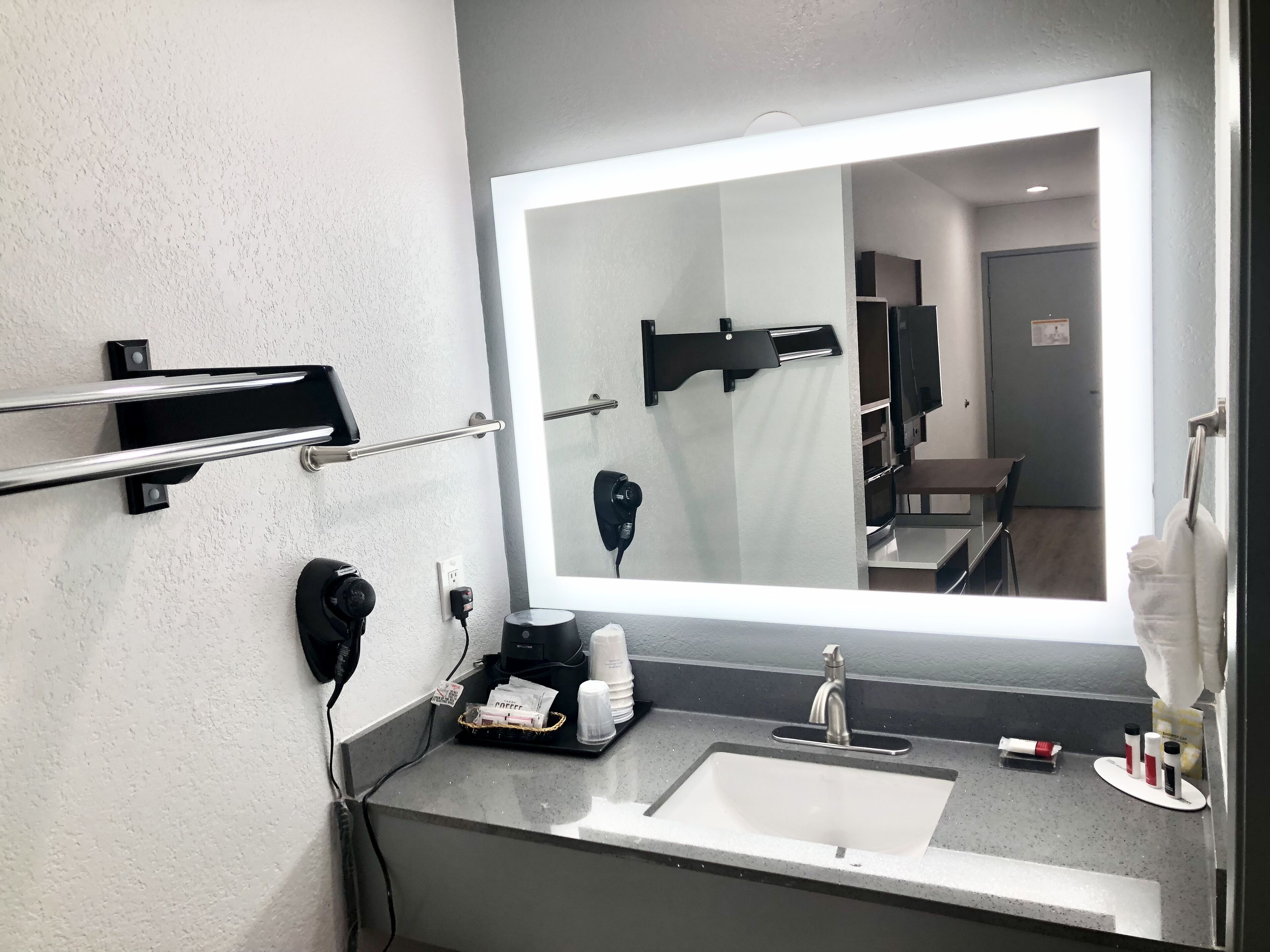 A modern bathroom with a large mirror, a sink, and a hairdryer mounted on the wall.