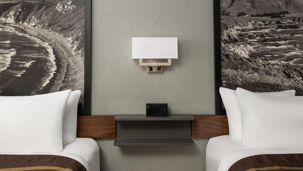 Una habitación de hotel con dos camas, una mesita de noche y un televisor instalado en la pared.