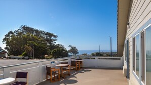 Un balcón con mobiliario exterior, vista al océano y un edificio con amplios ventanales.