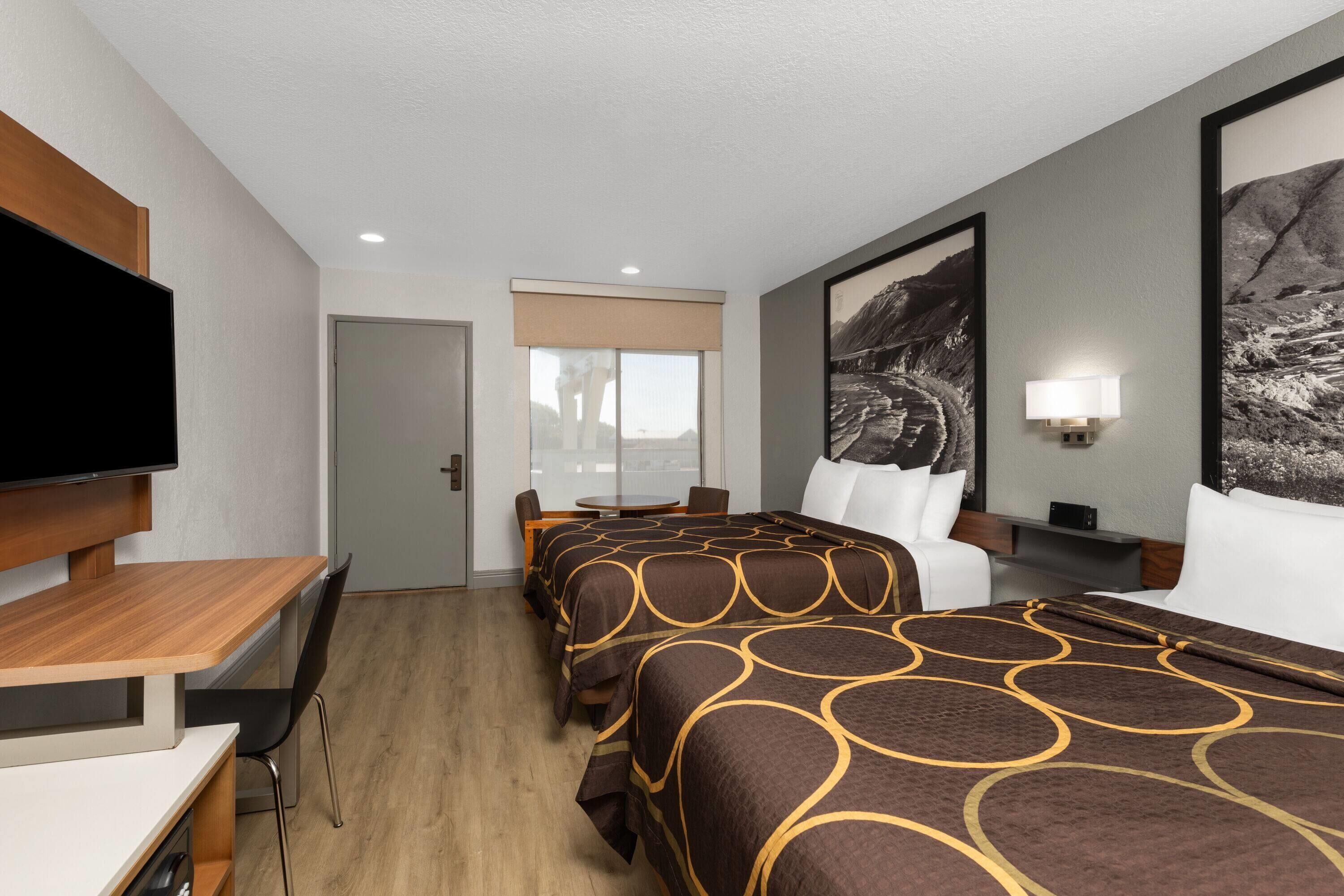 A hotel room with a bed, a desk, a chair, a TV, and a window.