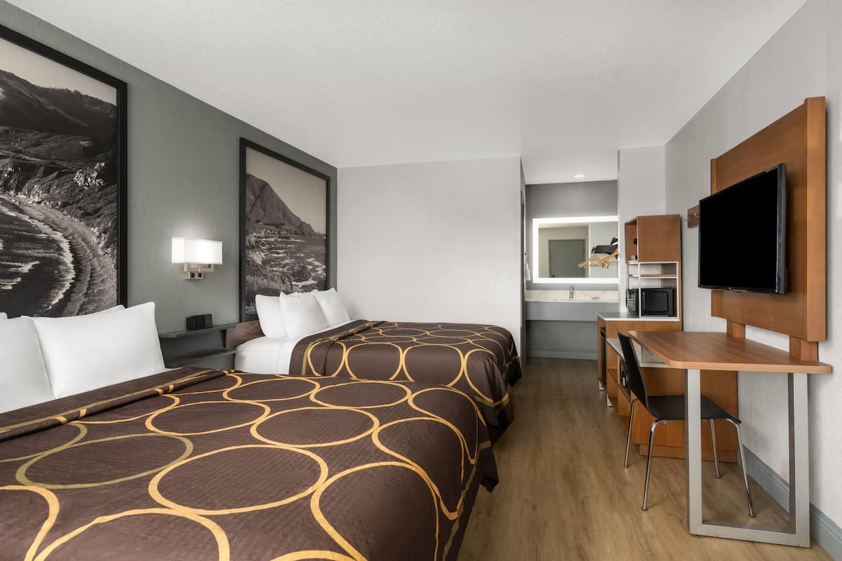 Ein Hotelzimmer mit zwei Betten, einem Schreibtisch, einem Fernseher und einem Badezimmer im Hintergrund.