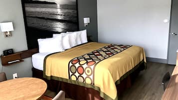 A hotel room with a bed, a desk, a chair, a round table, and a large painting of a beach scene.