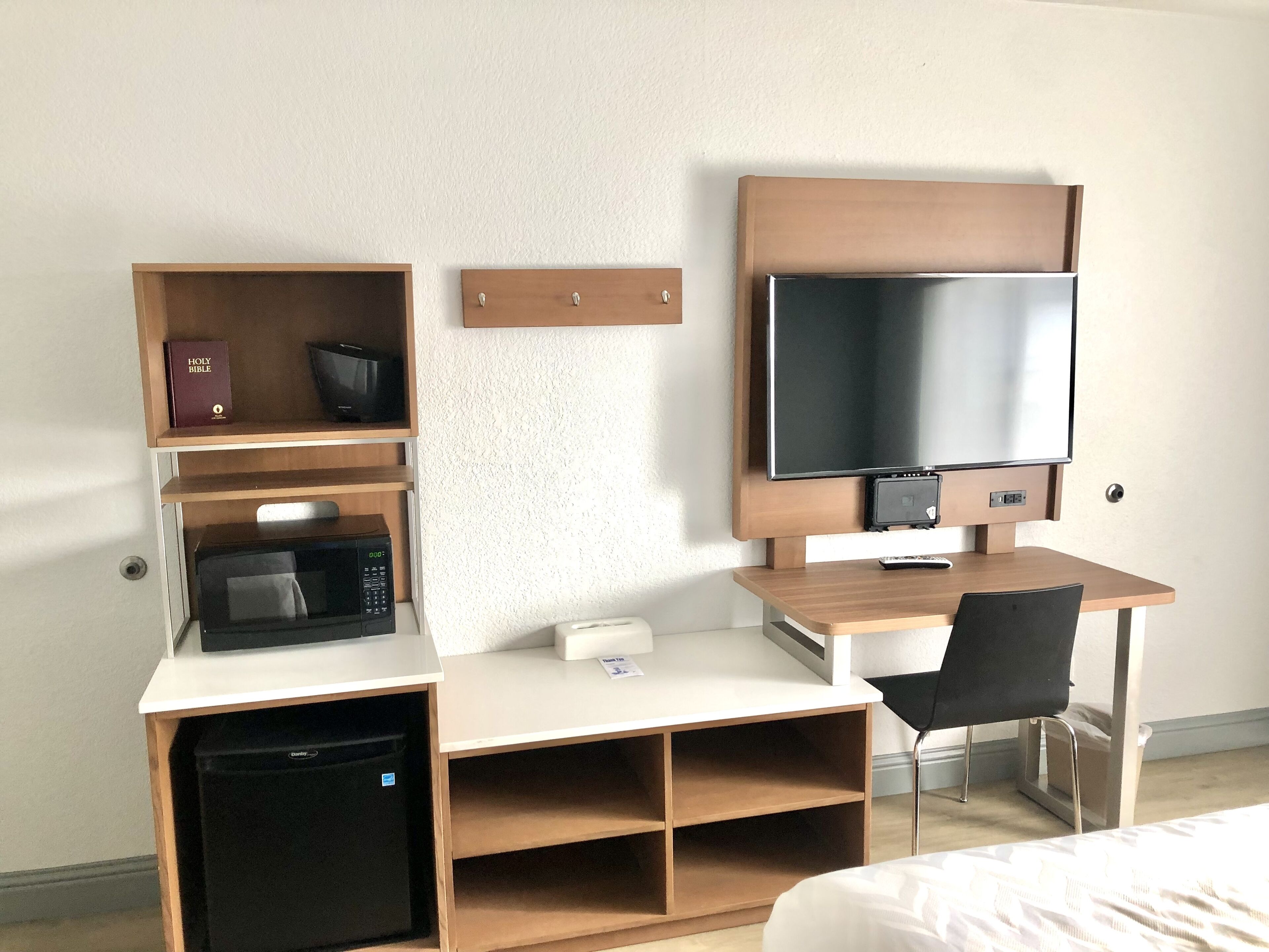 A compact hotel room with a wooden desk, a television, a microwave, and a small refrigerator.