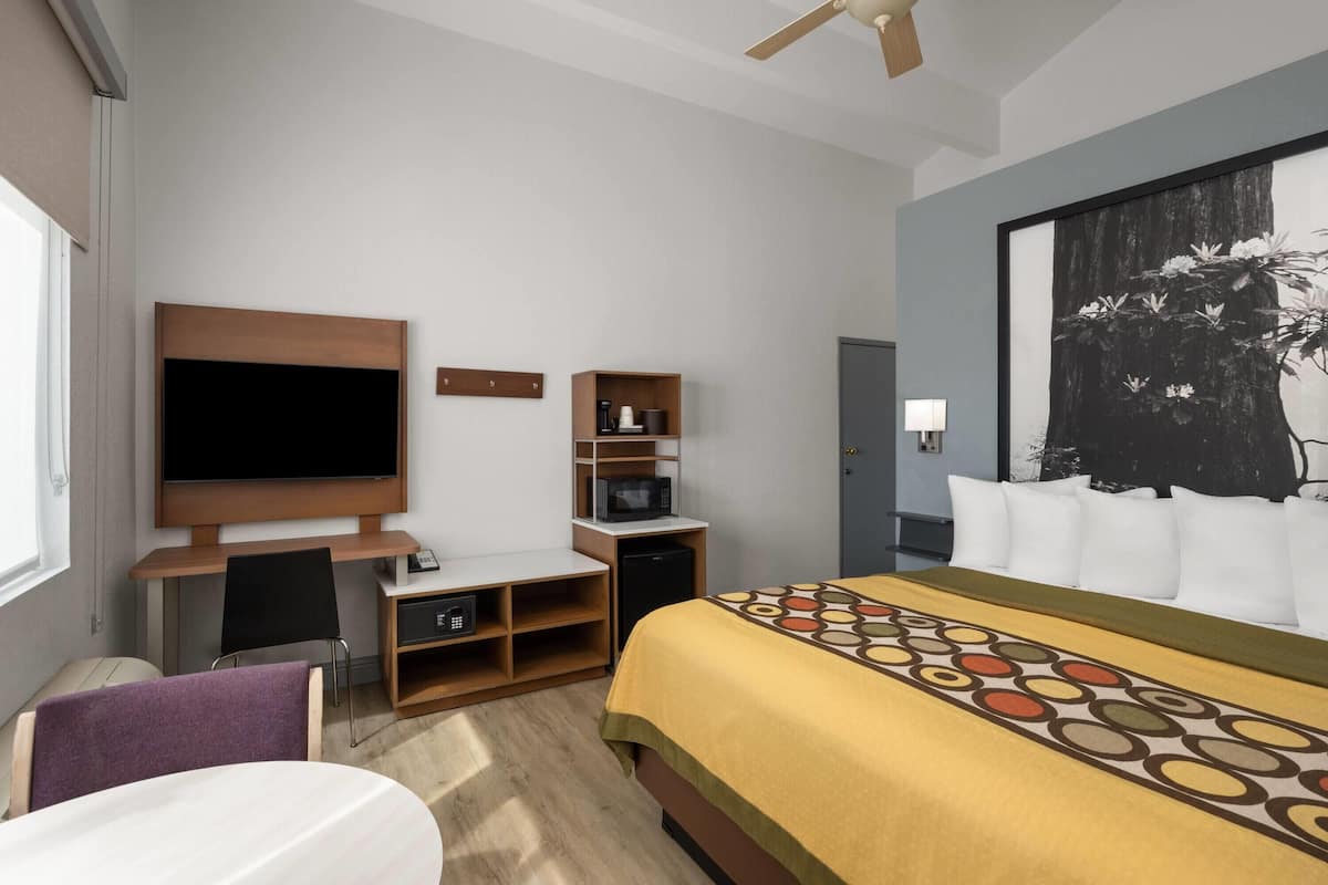 Ein Hotelzimmer mit Bett, Schreibtisch, Fernseher, Mikrowelle und einem großen Gemälde an der Wand.
