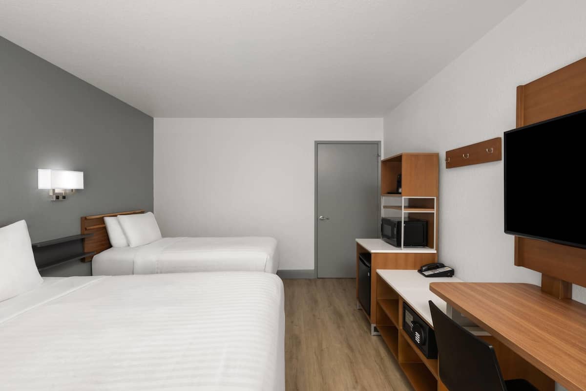 Ein modernes Hotelzimmer mit zwei Betten, einem Schreibtisch, einem Fernseher und einem Kleiderschrank.