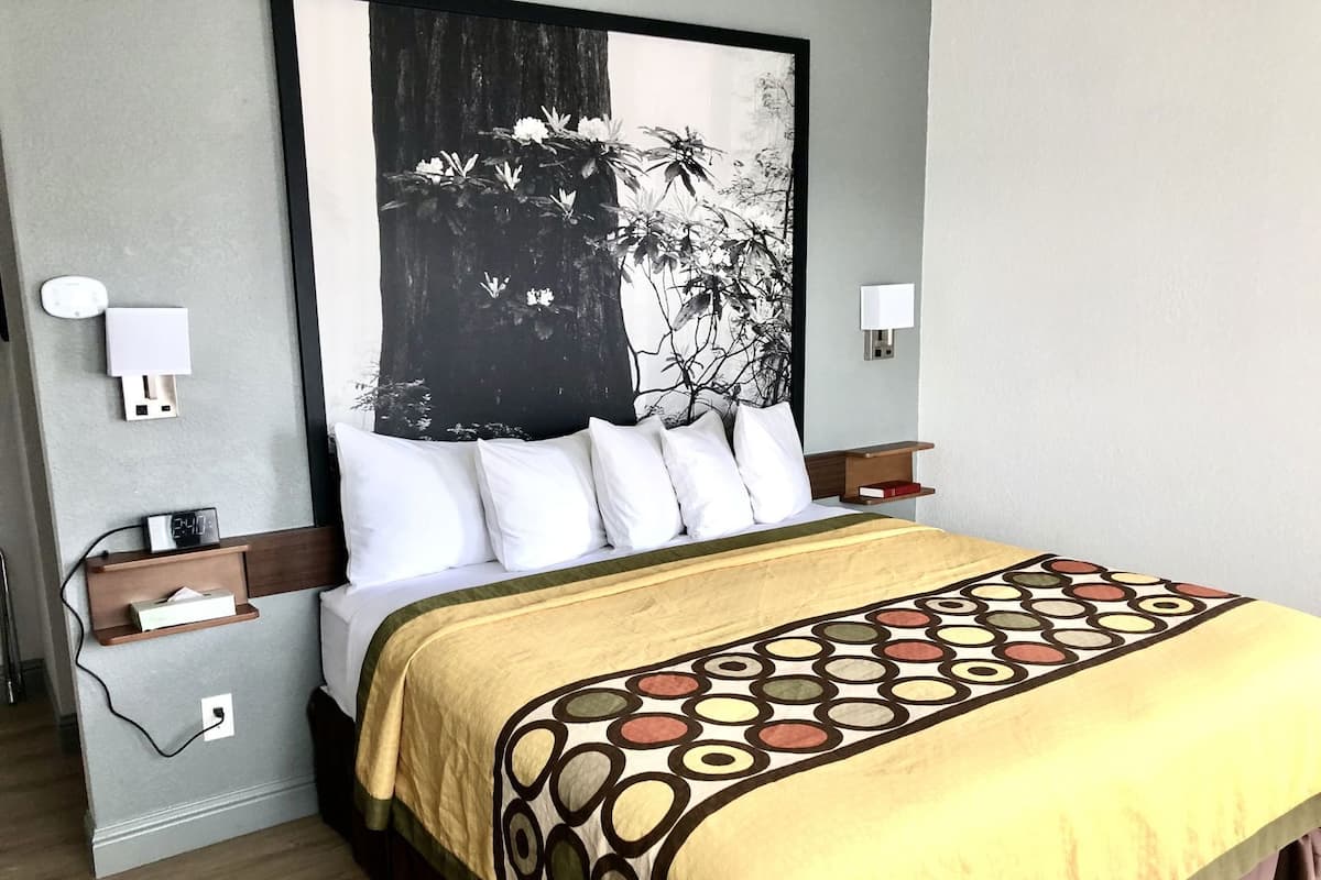 Ein Hotelzimmer mit einem Bett, einer großen schwarz-weißen Blumenarbeit an der Wand, Nachttischen mit Lampen und einem Holznachttisch.