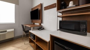 Una habitación de hotel moderna con un escritorio de madera, un televisor de pantalla plana, un microondas y una cafetera.