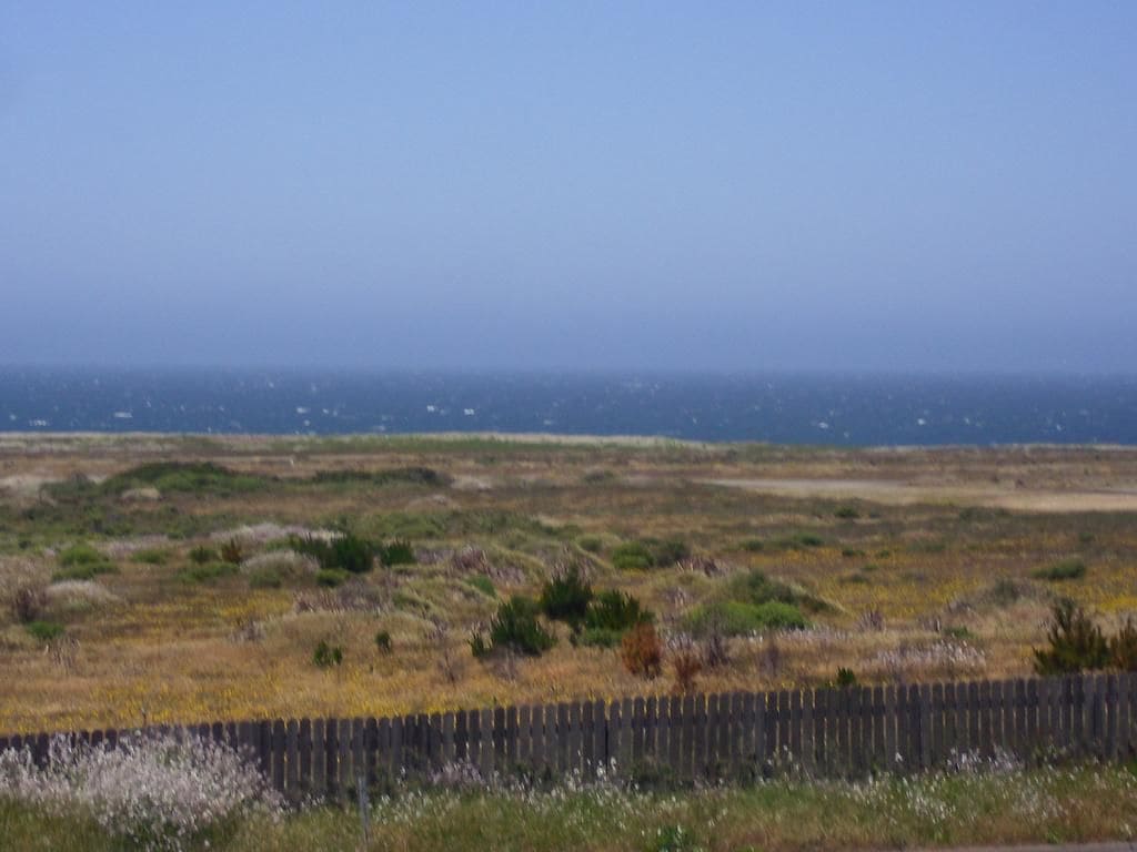 Paisaje costero con una valla de madera al frente y una vista despejada del océano al fondo.