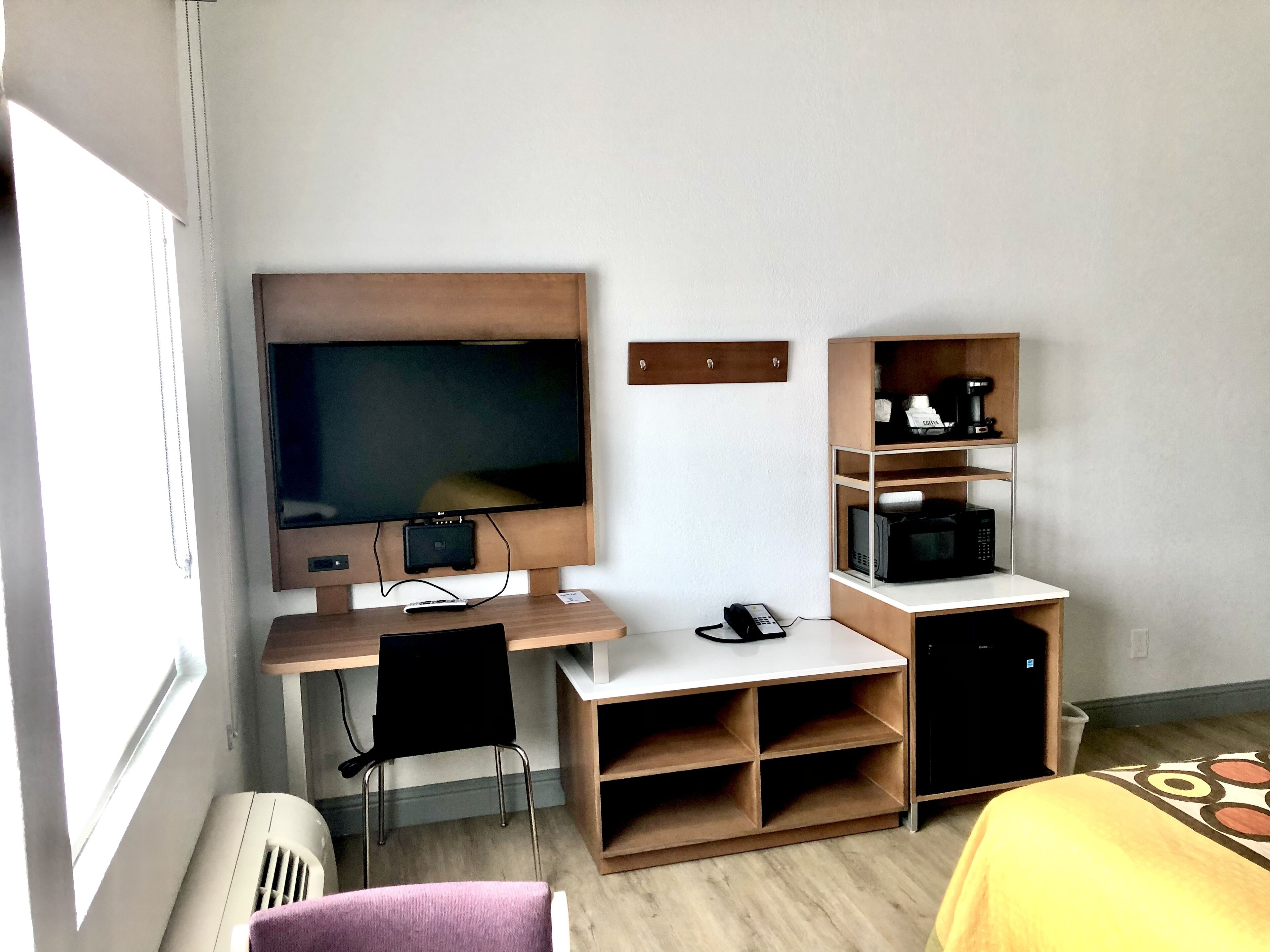 Una habitación de hotel con televisor, escritorio con silla, microondas, cafetera y cama con colcha estampada.