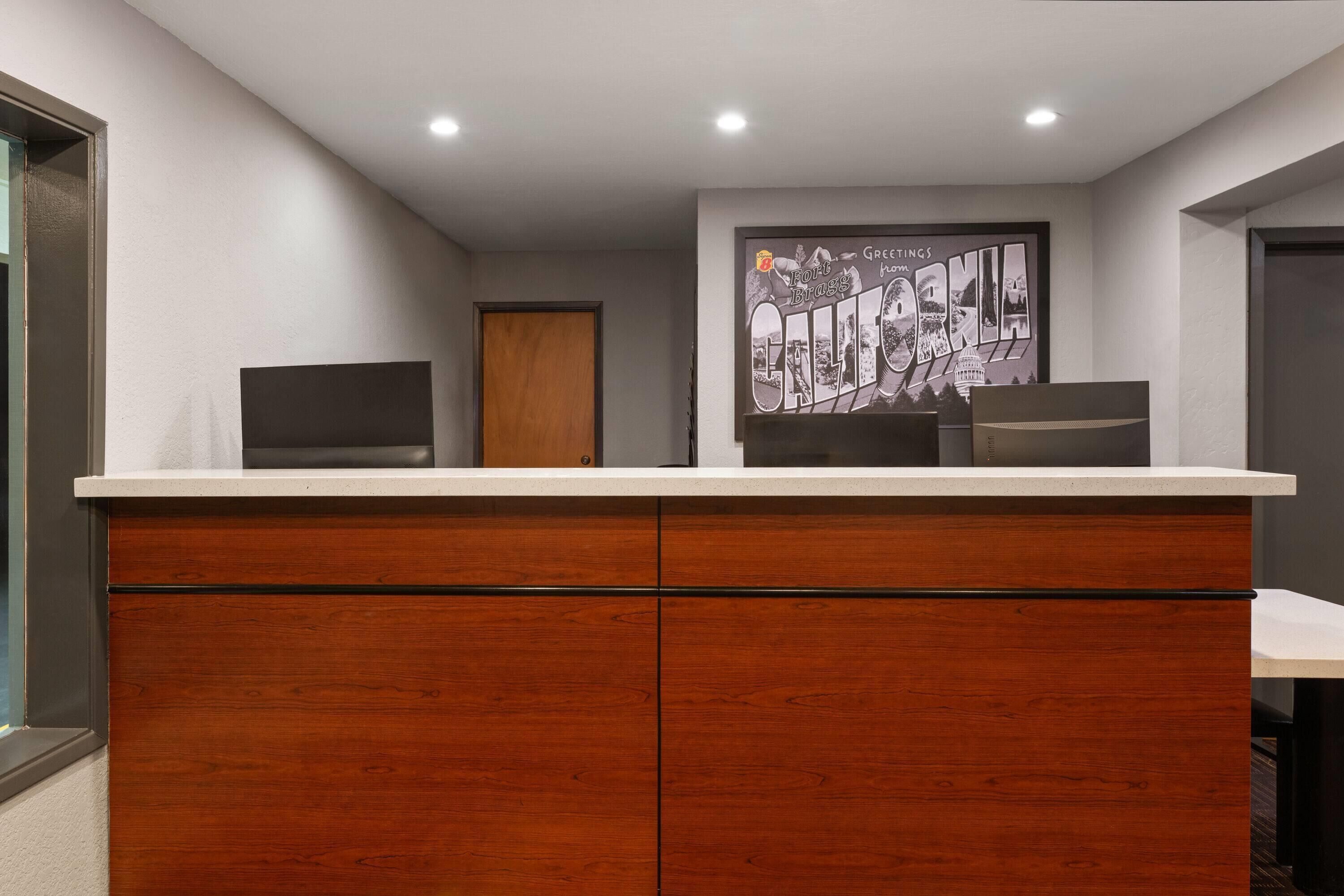 A reception desk with a wooden cabinet, a framed cityscape poster, and a door in the background.