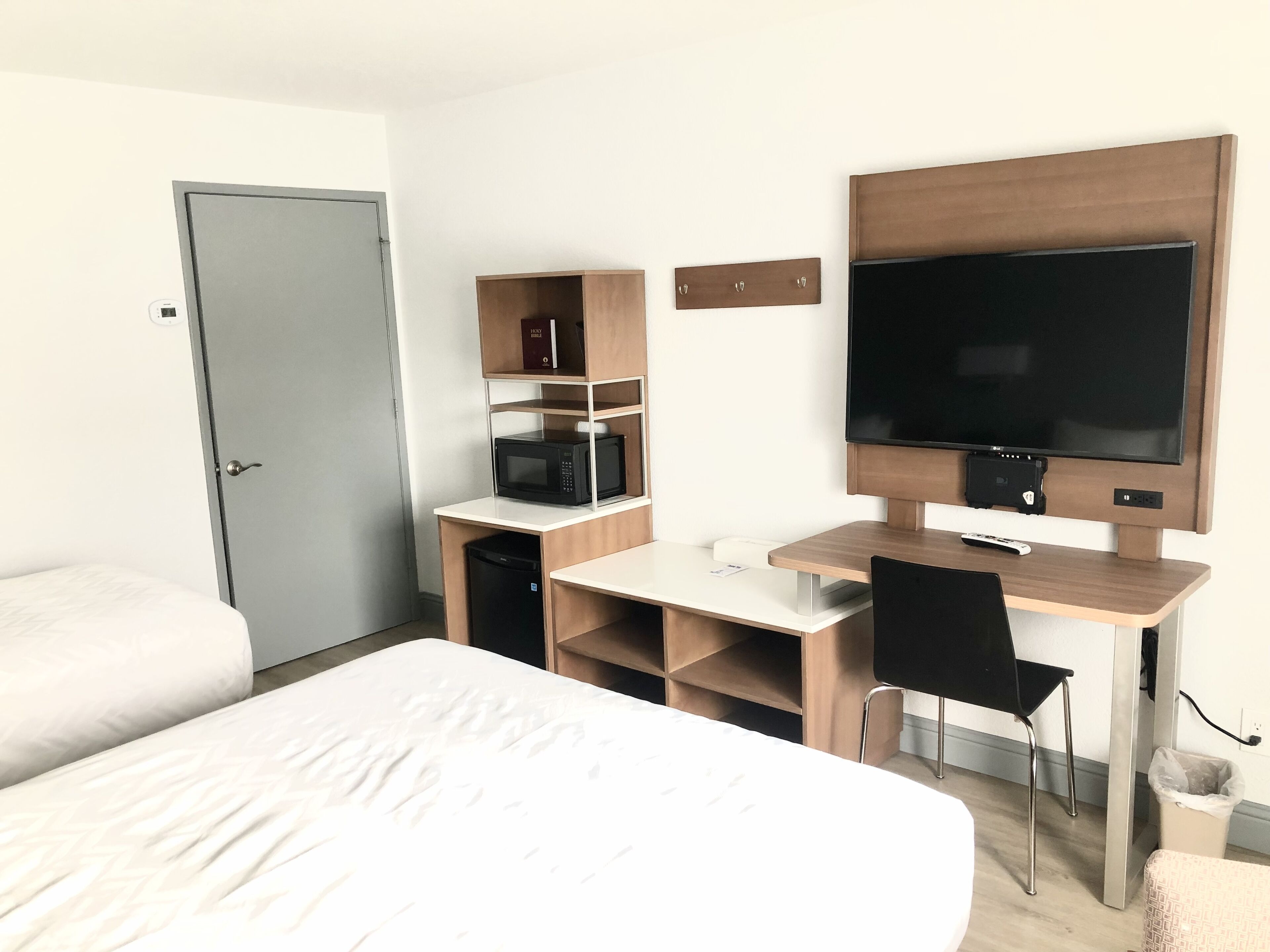 A hotel room with a bed, a desk with a chair, a television, a microwave, and a bookshelf.