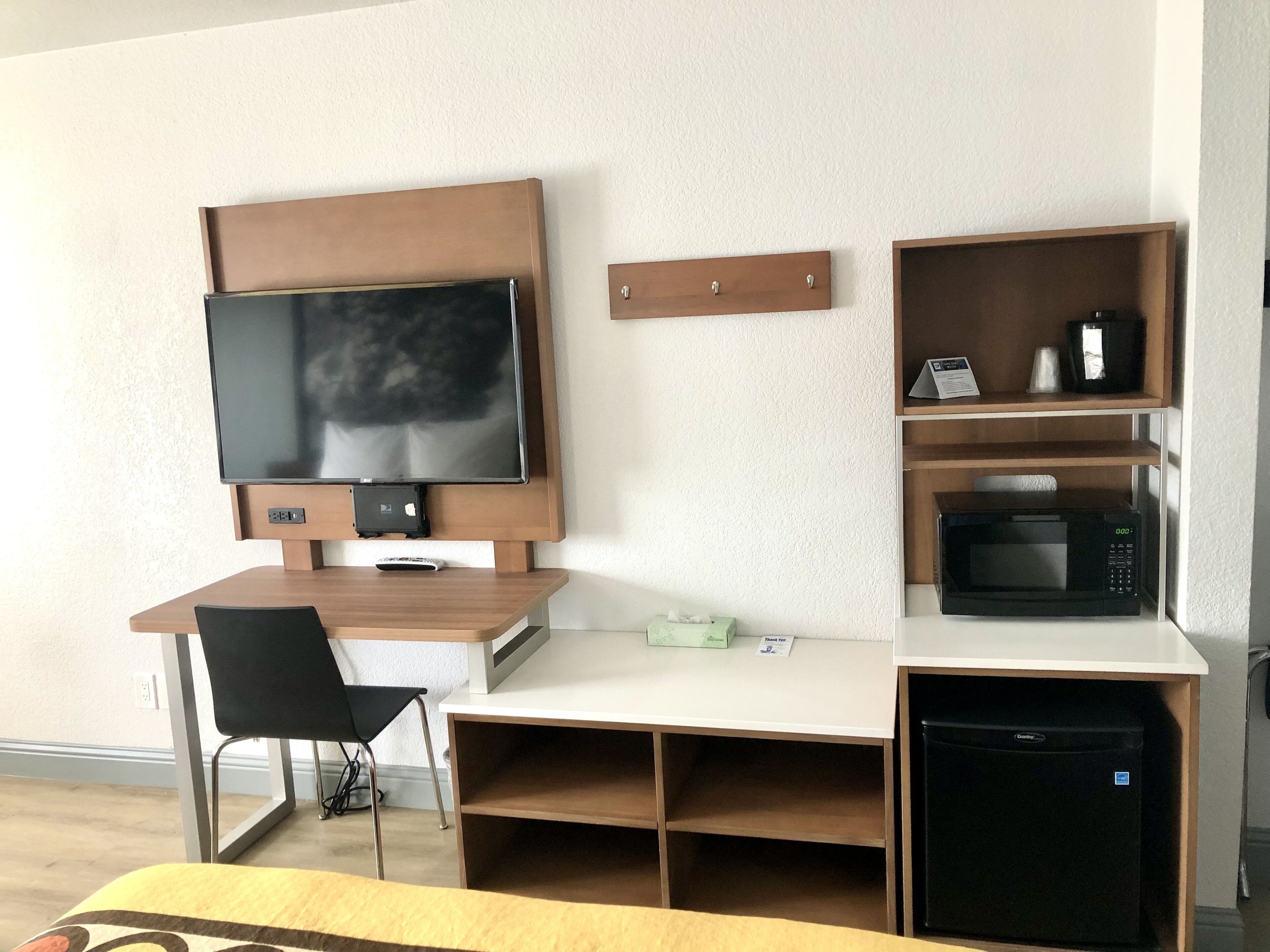 A compact hotel room with a wooden desk, a television, a microwave, and a small refrigerator.