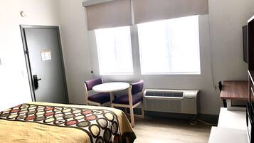 A hotel room with a bed, a desk, a chair, an air conditioner, and a window with blinds.