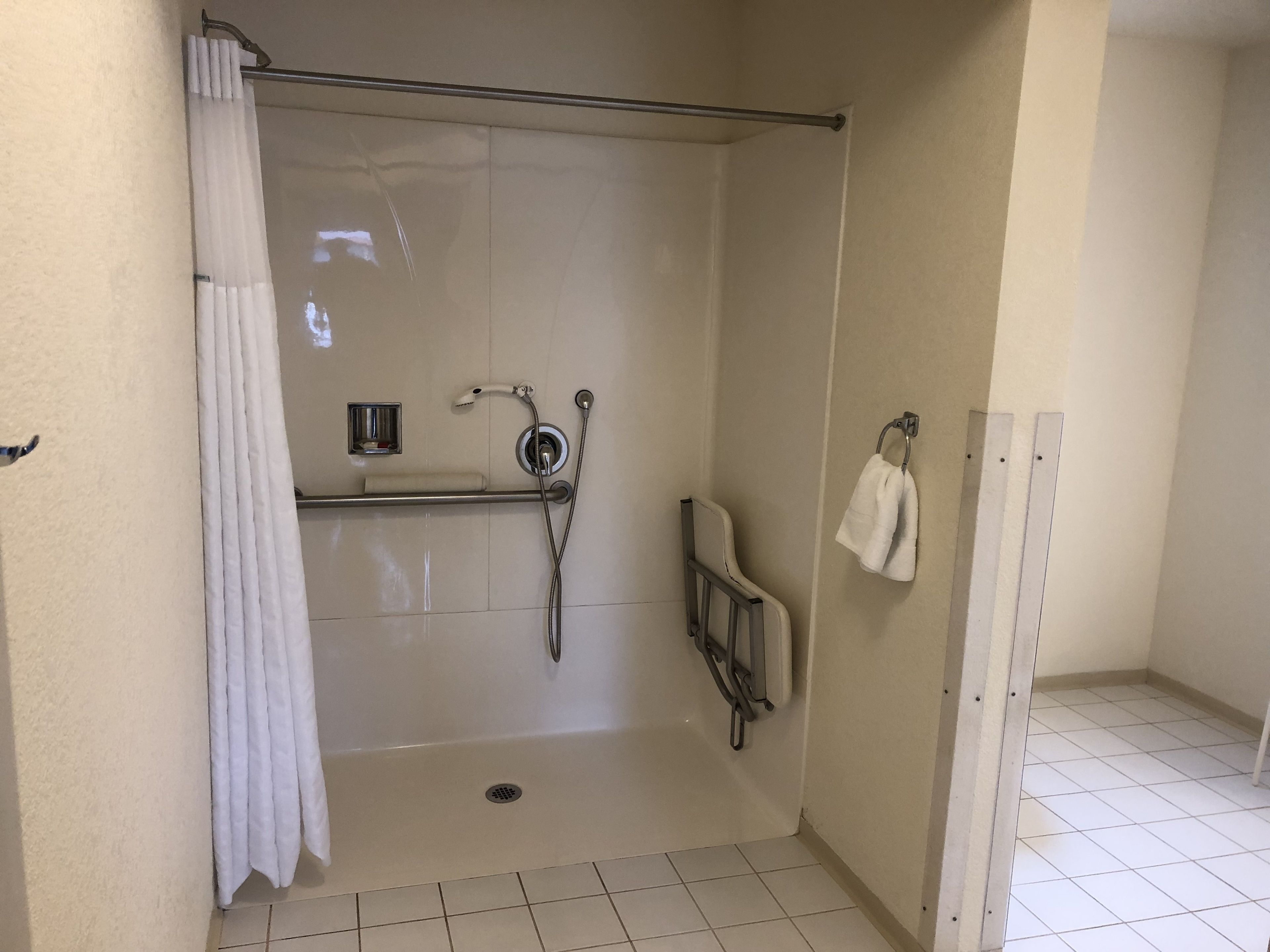 A small, enclosed shower area with a white curtain, a handheld showerhead, a towel rack, and a small shelf with a soap dish.