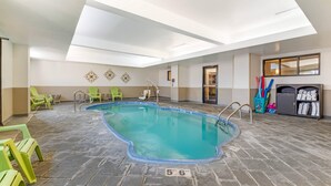An indoor swimming pool with a skylight ceiling, green chairs, and a towel rack.